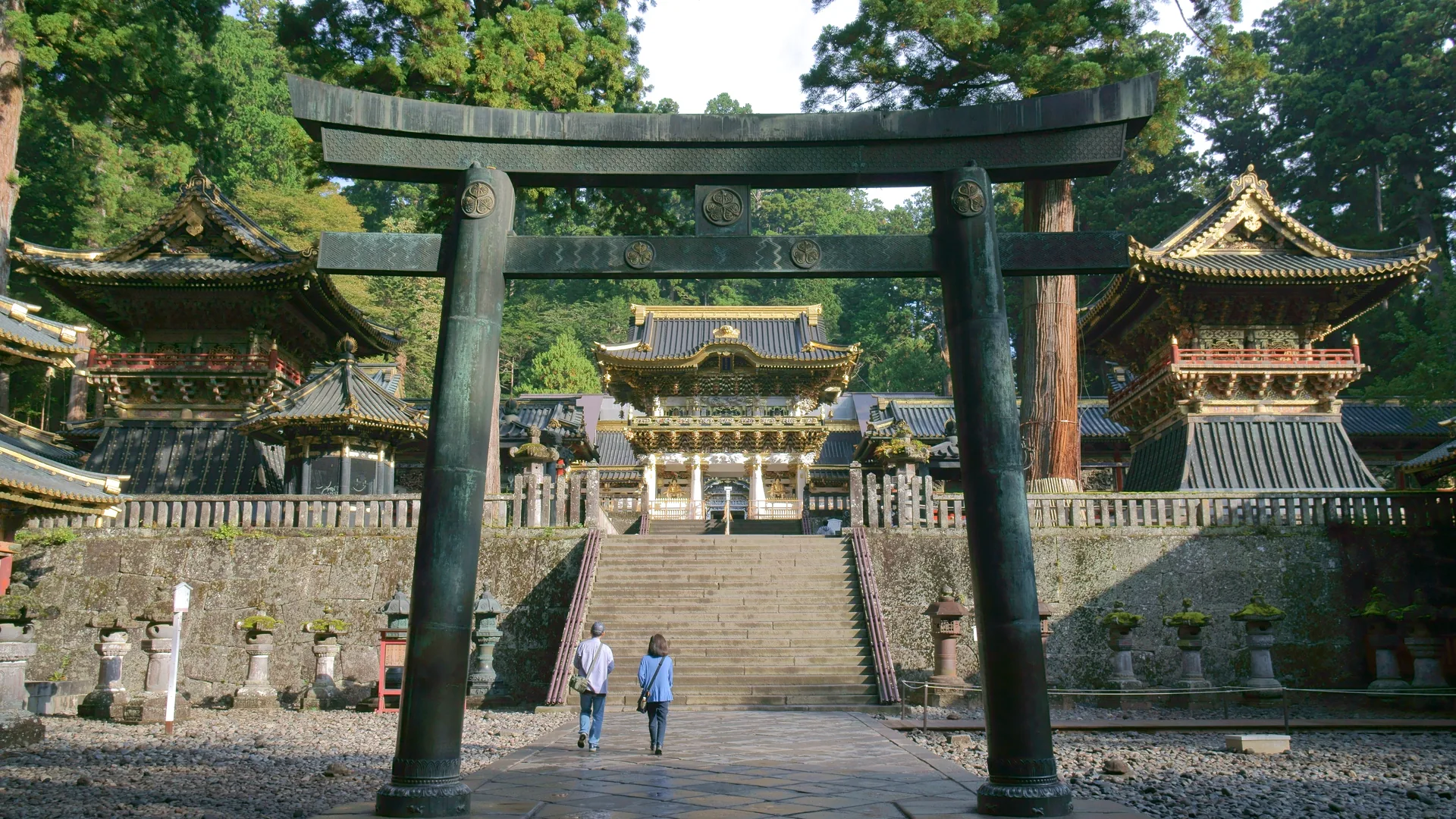 The stone torii gate and gilded Yomeimon Gate at Nikko Toshogu Shrine, seen through cedar trees